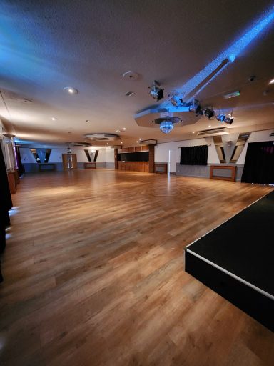A spacious, well-lit event hall with wooden flooring and a projector.